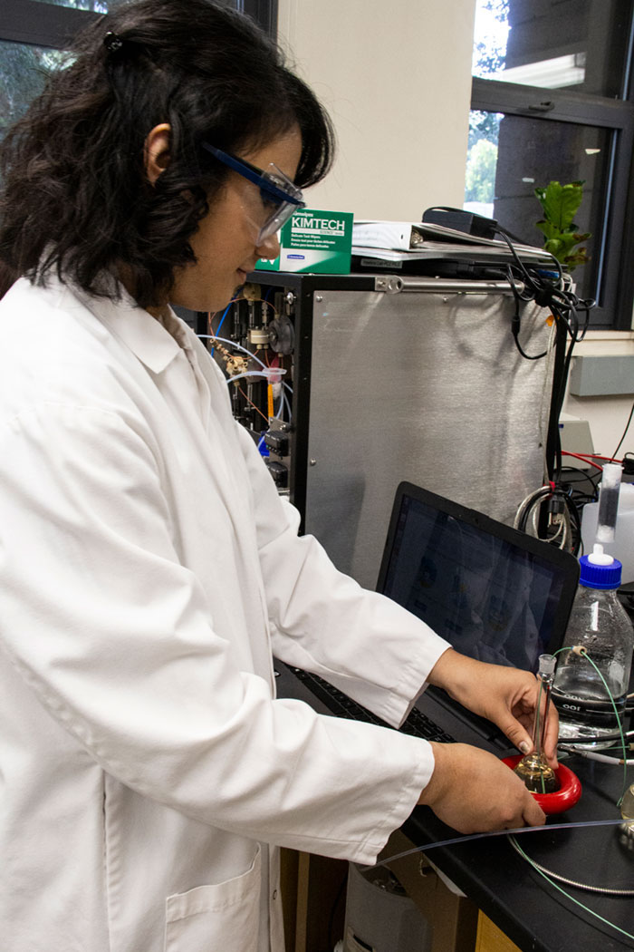 Student in lab coat works with testing device.