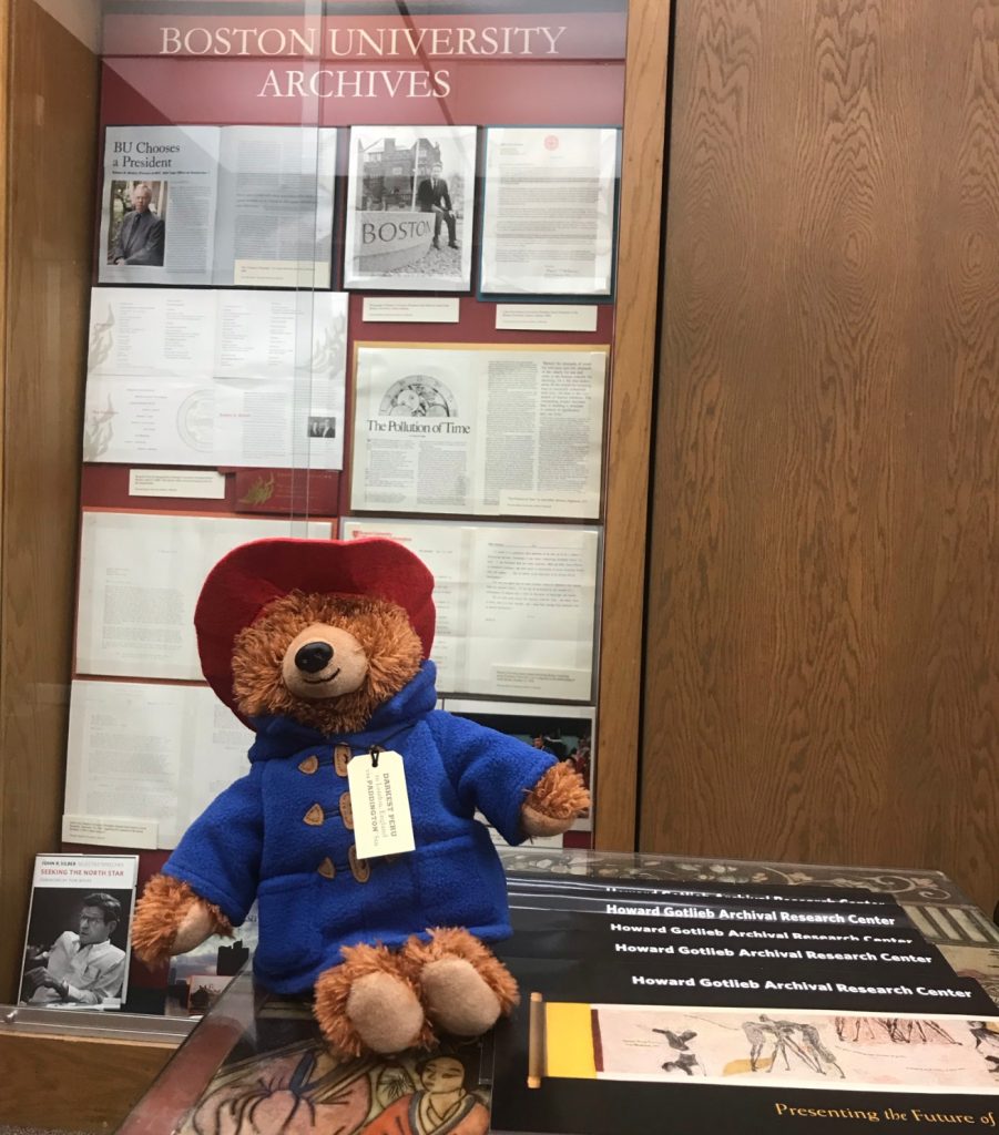 Paddington Bear sits among items in a library.