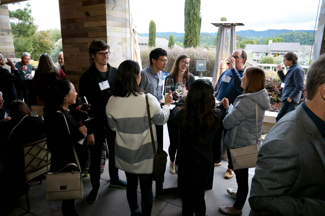 Group of people stand around table socializing.