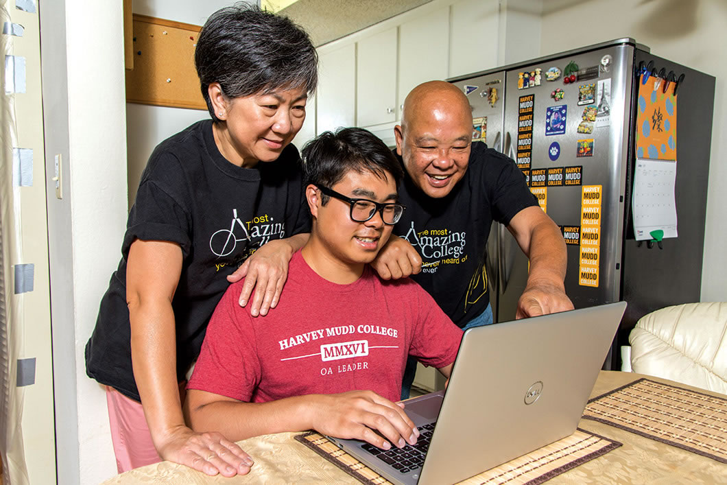 Lam sits at desk looking at laptop as his parents look over his shoulder.