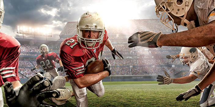 Football player runs toward camera as opposing team try to tackle him.