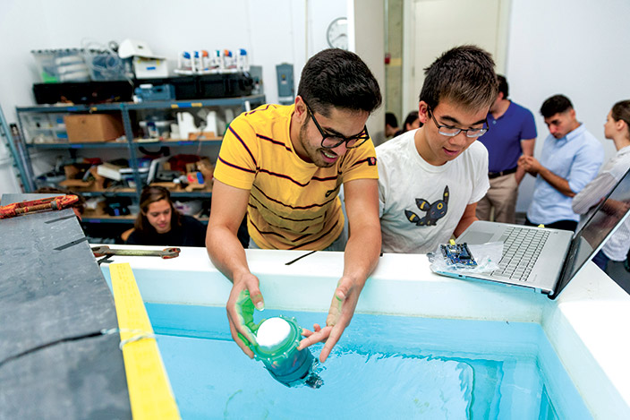 Two students test device in water tank.