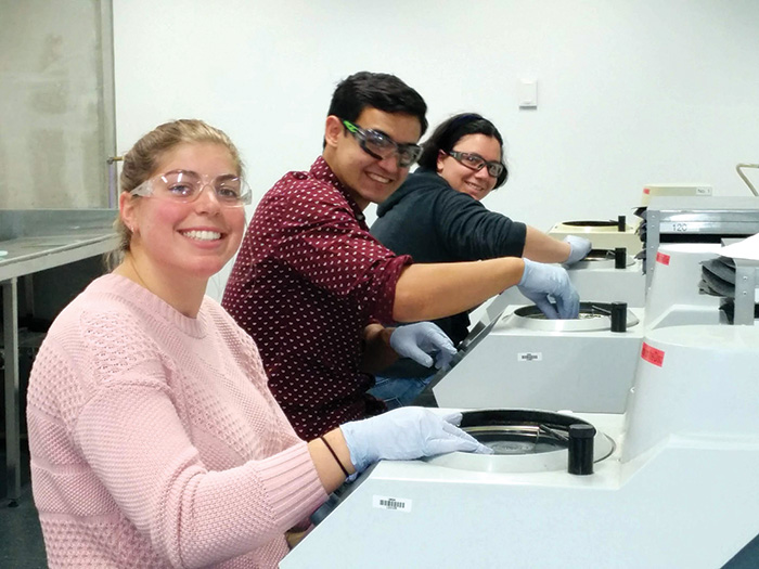 Three students at wearing gloves working on samples in testing machines.