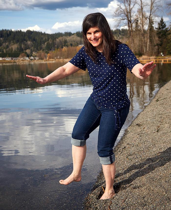 Julia with jeans rolled up stands poised to step in a pond.