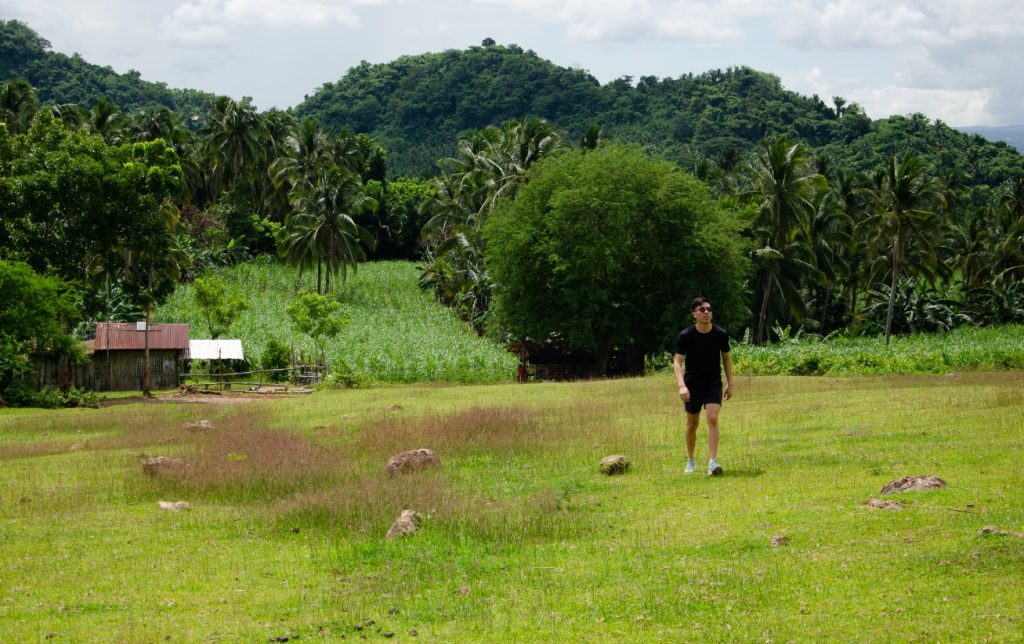 Fernando Salud walks across open grass with wooded hill in background.